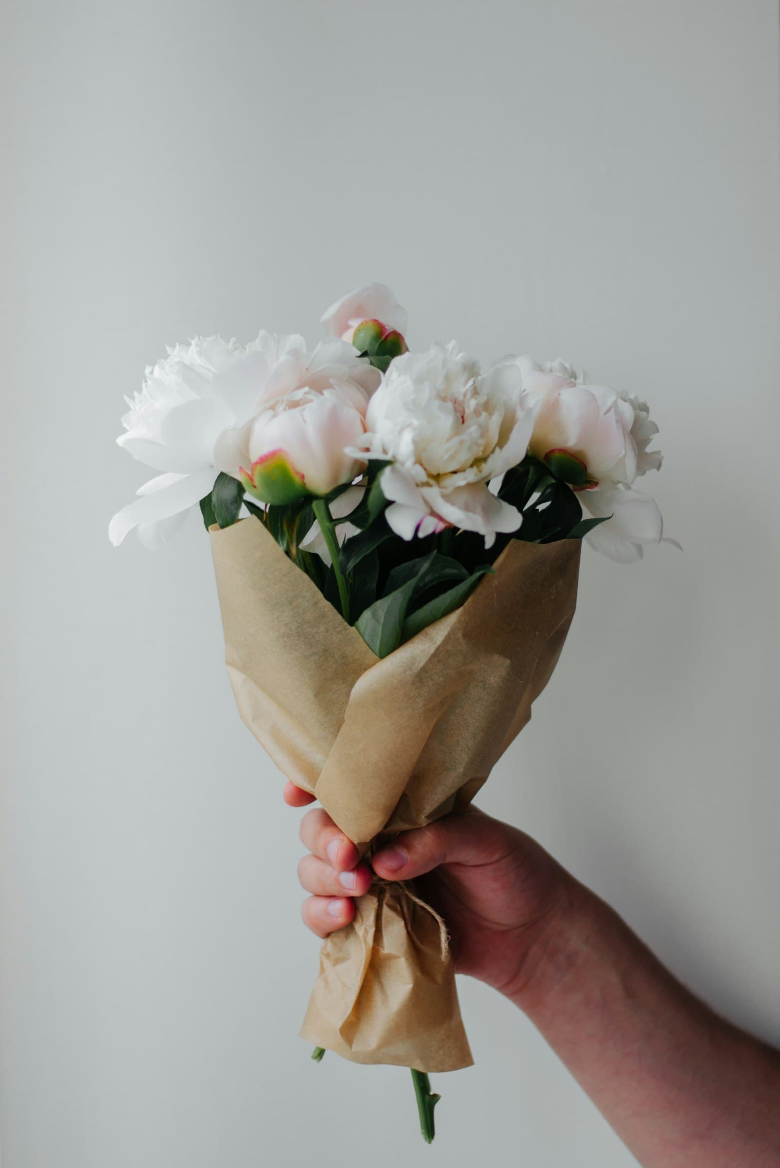 Kraft-wrapped peonies held up against a soft grey wall
